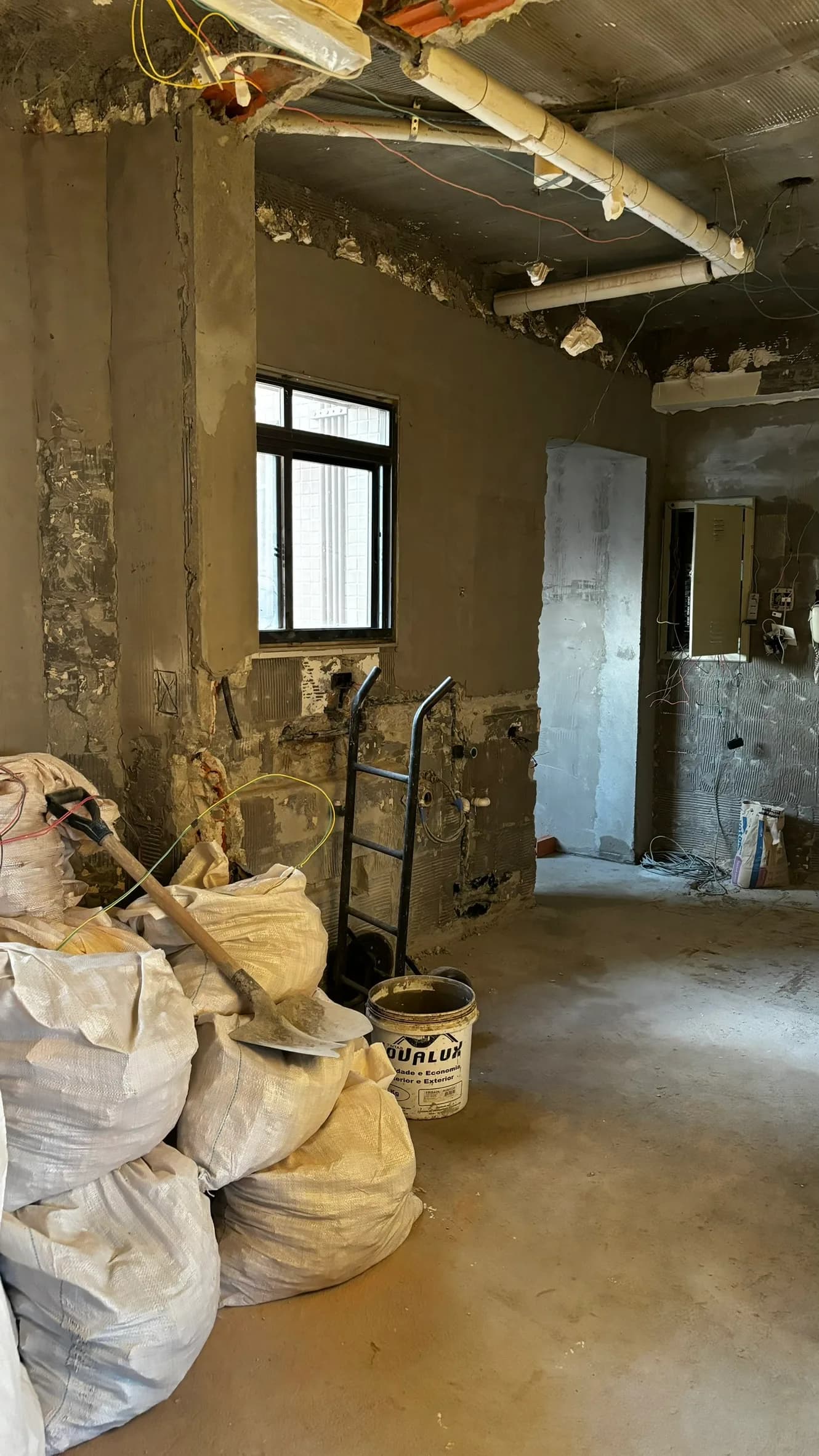 Apartamento em obra, com paredes demolidas, tubulações expostas e sacos de entulho