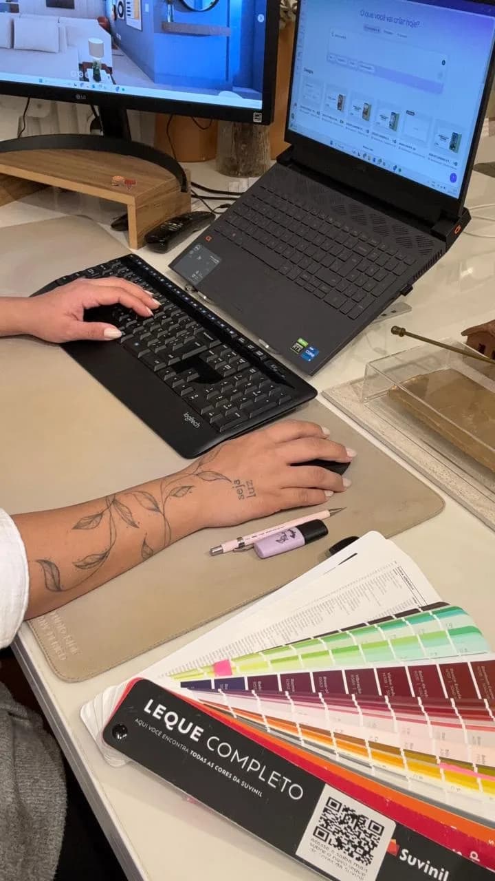 Mesa de trabalho com notebook, monitores e um leque de cores aberto