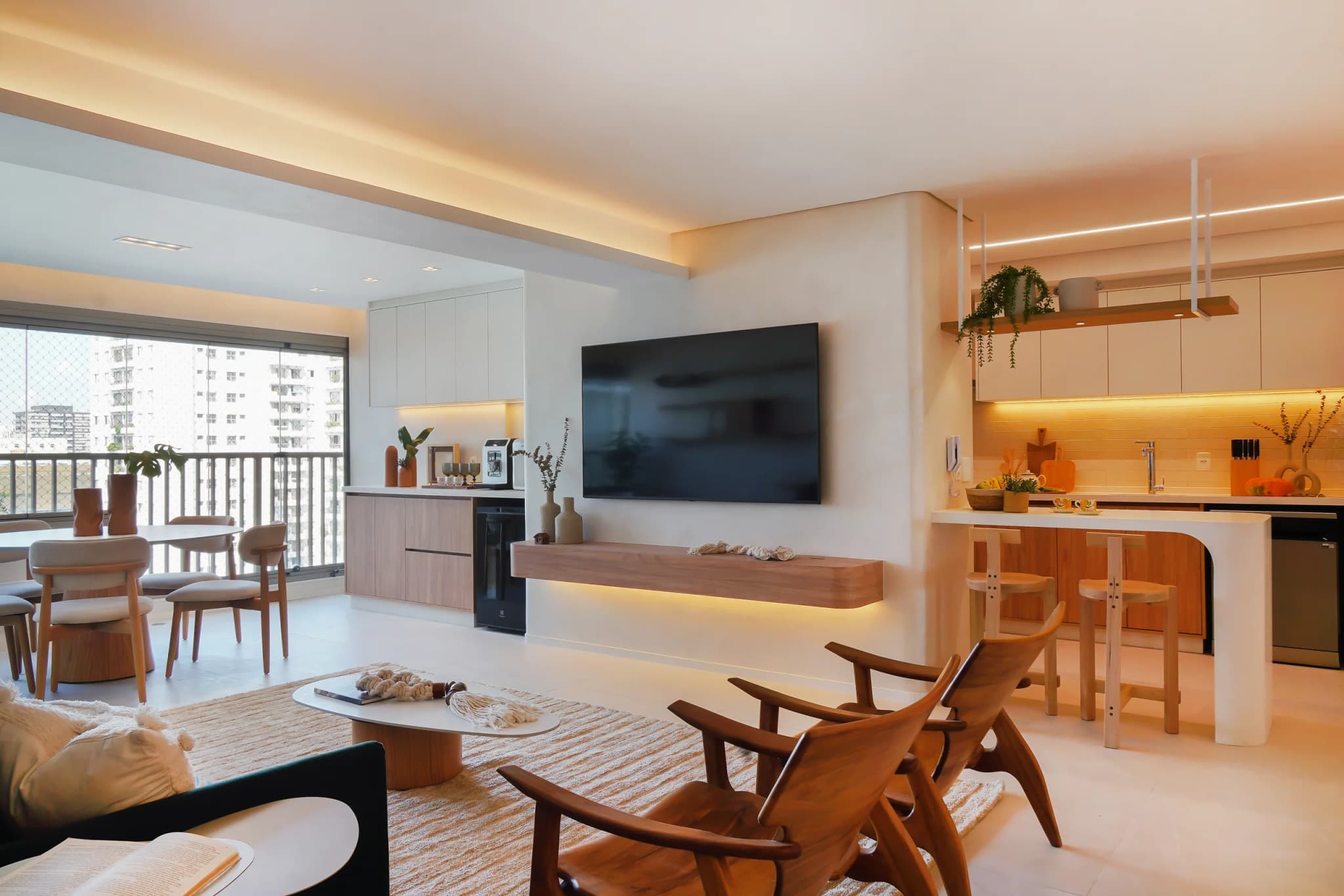 Sala do Apê Colômbia integrada à cozinha, com painel da TV, bancada de refeições e varanda ao fundo